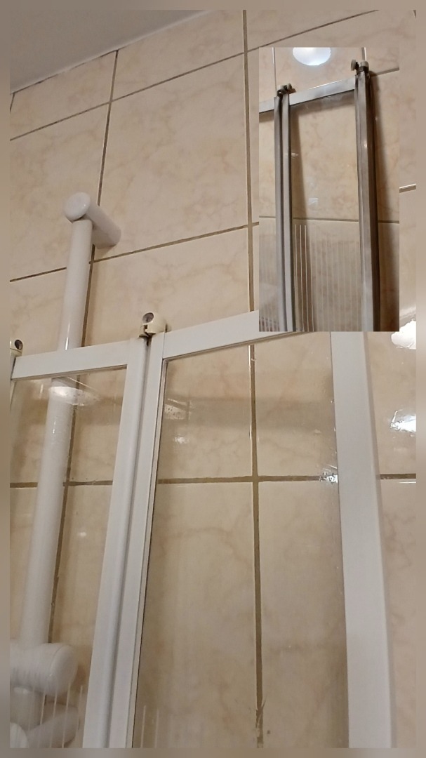 Biała kabina prysznicowa z widocznymi śladami użytkowania na kafelkach i uszczelkach. Widoczne zacieki i osady. Kątowe ujęcie.