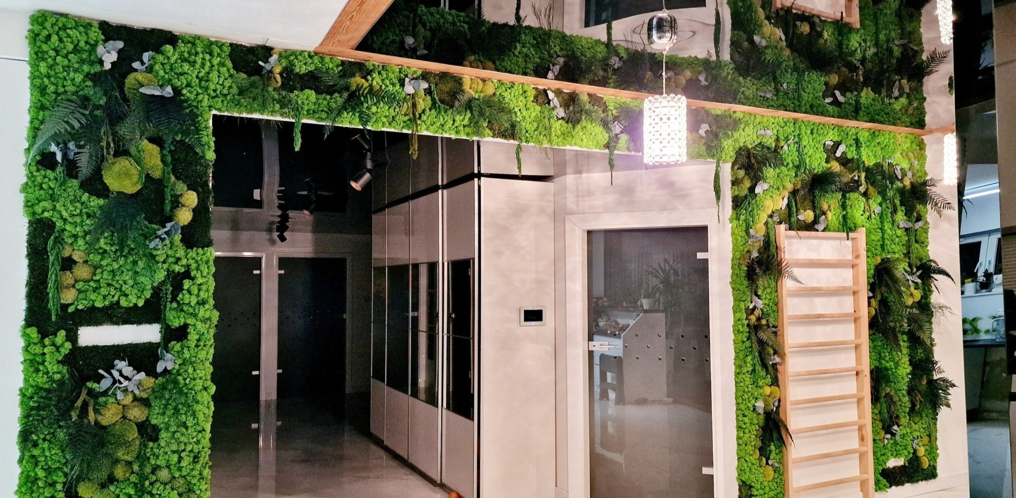 Nowoczesne wnętrze z pionowymi panelami z mchu i roślin, drewniana drabina dekoracyjna, szklane drzwi i szafy w tle, oświetlenie punktowe i wisząca lampa.
