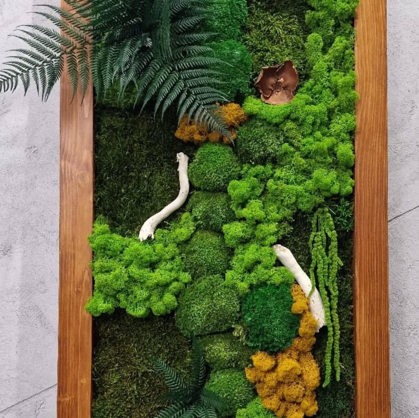 Panel ścienny z mchu w drewnianej ramie, z dodatkiem paproci, gałązek i suszonych kwiatów, różne odcienie zieleni i żółci.