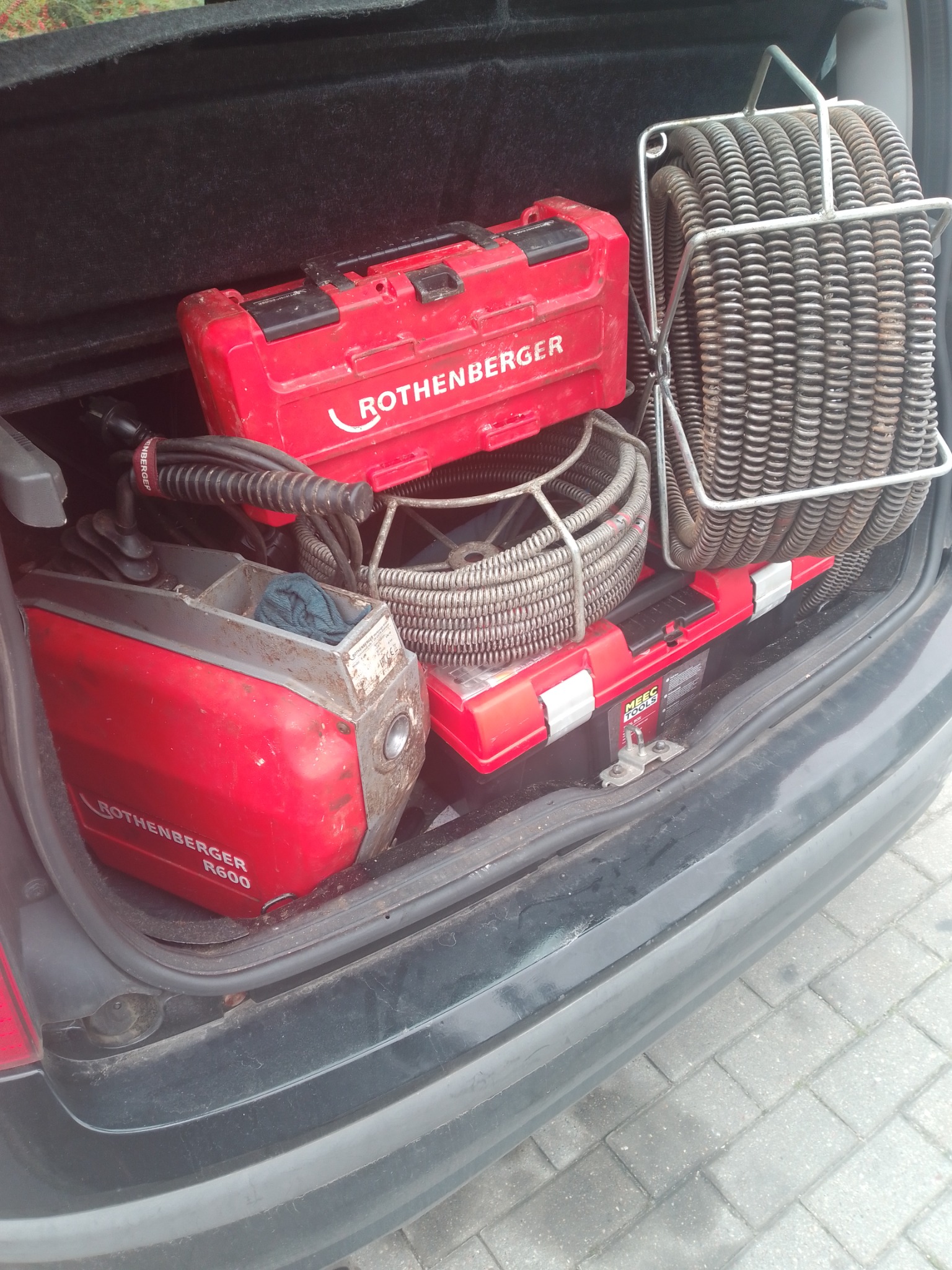 Sprzęt hydrauliczny Rothenberger w bagażniku auta: maszyna R600, spirale do udrażniania rur i skrzynka narzędziowa. Widok z góry na wyposażenie pogotowia hydraulicznego.