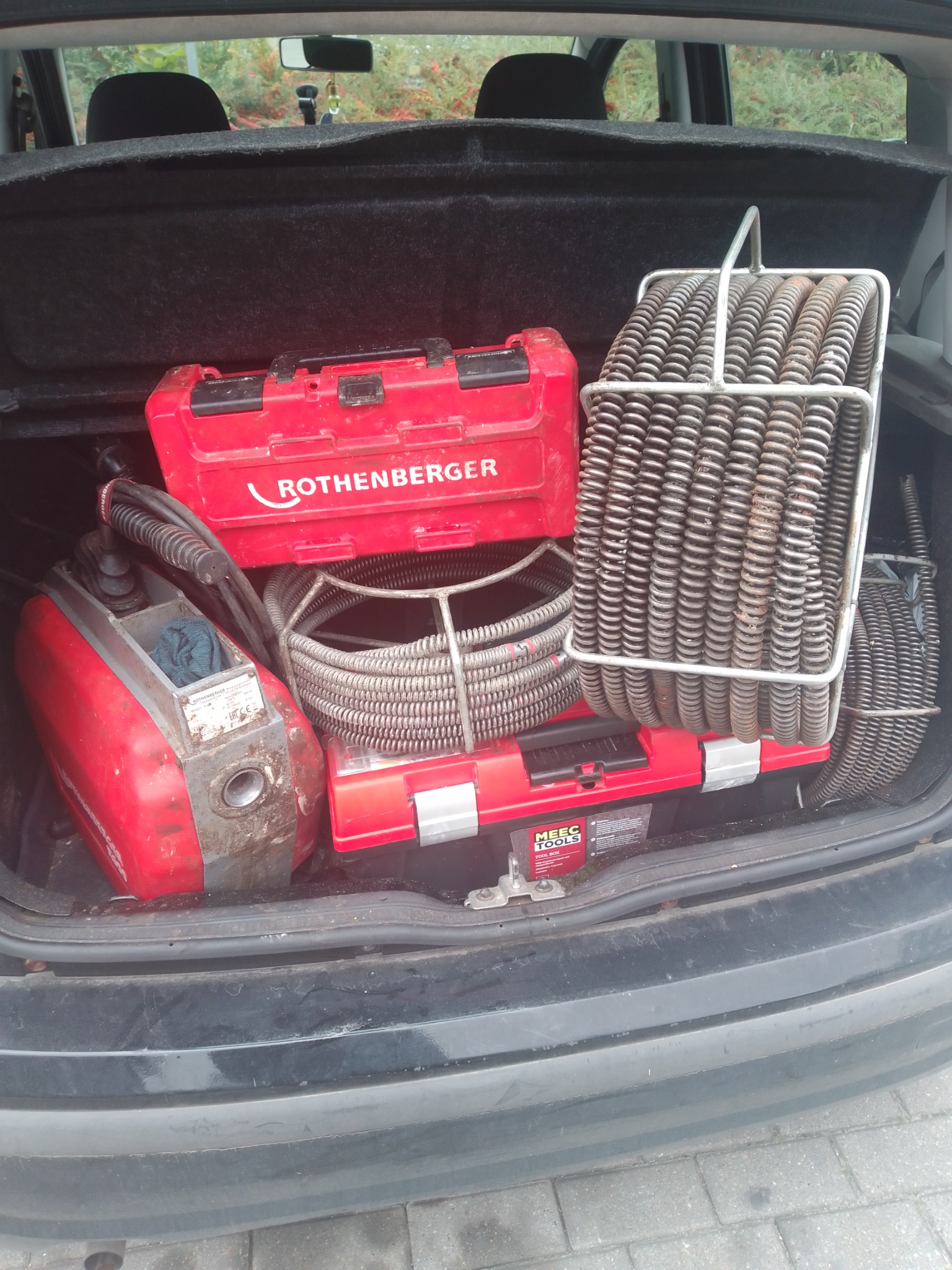 Sprzęt hydrauliczny Rothenberger w bagażniku samochodu: spirala do udrażniania rur, skrzynka narzędziowa i urządzenie czyszczące. Widok z góry na narzędzia pracy.