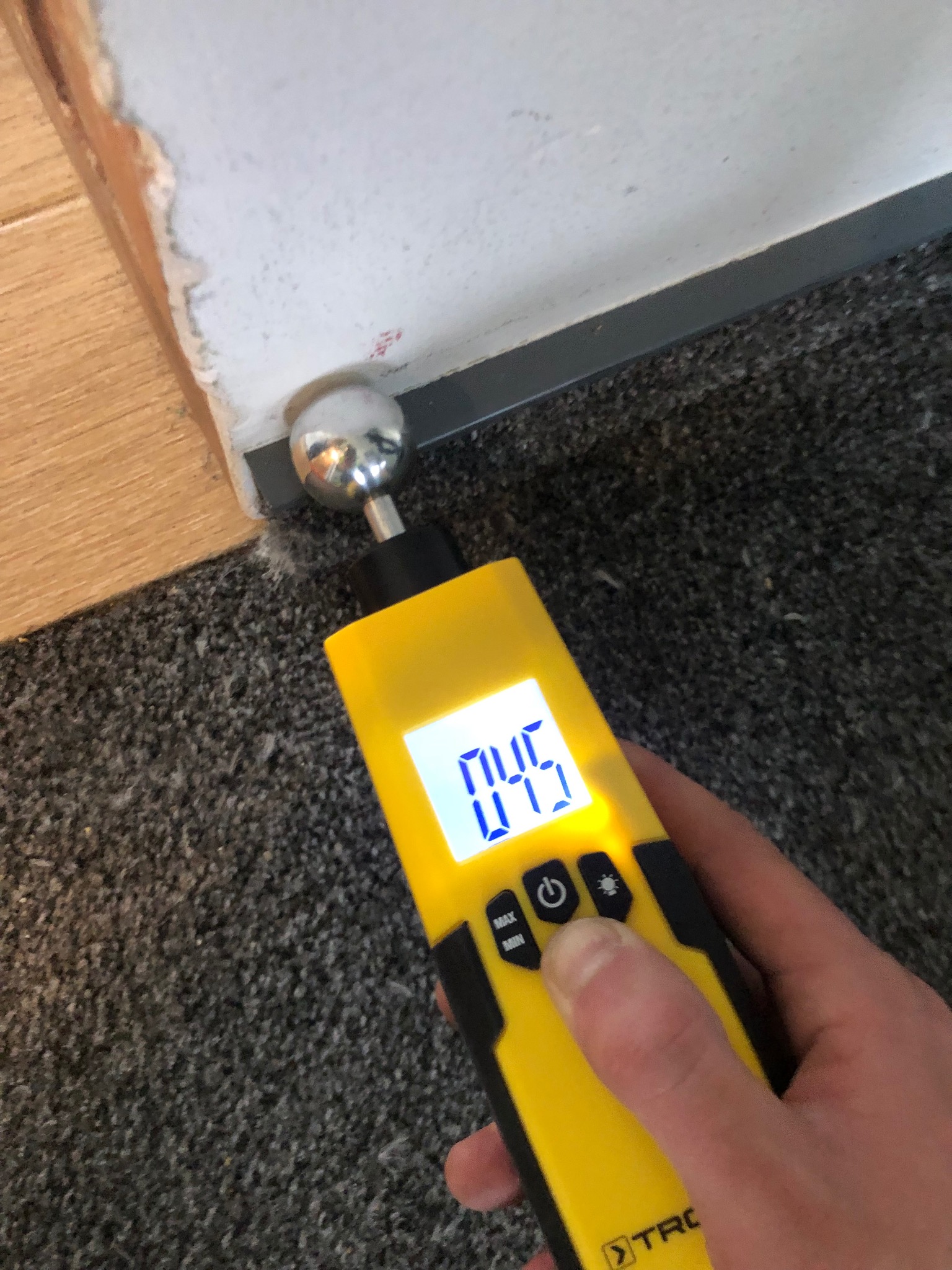 Pomiar wilgotności ściany przy podłodze za pomocą elektronicznego wilgotnościomierza marki Trotec, wskazującego wartość 045.