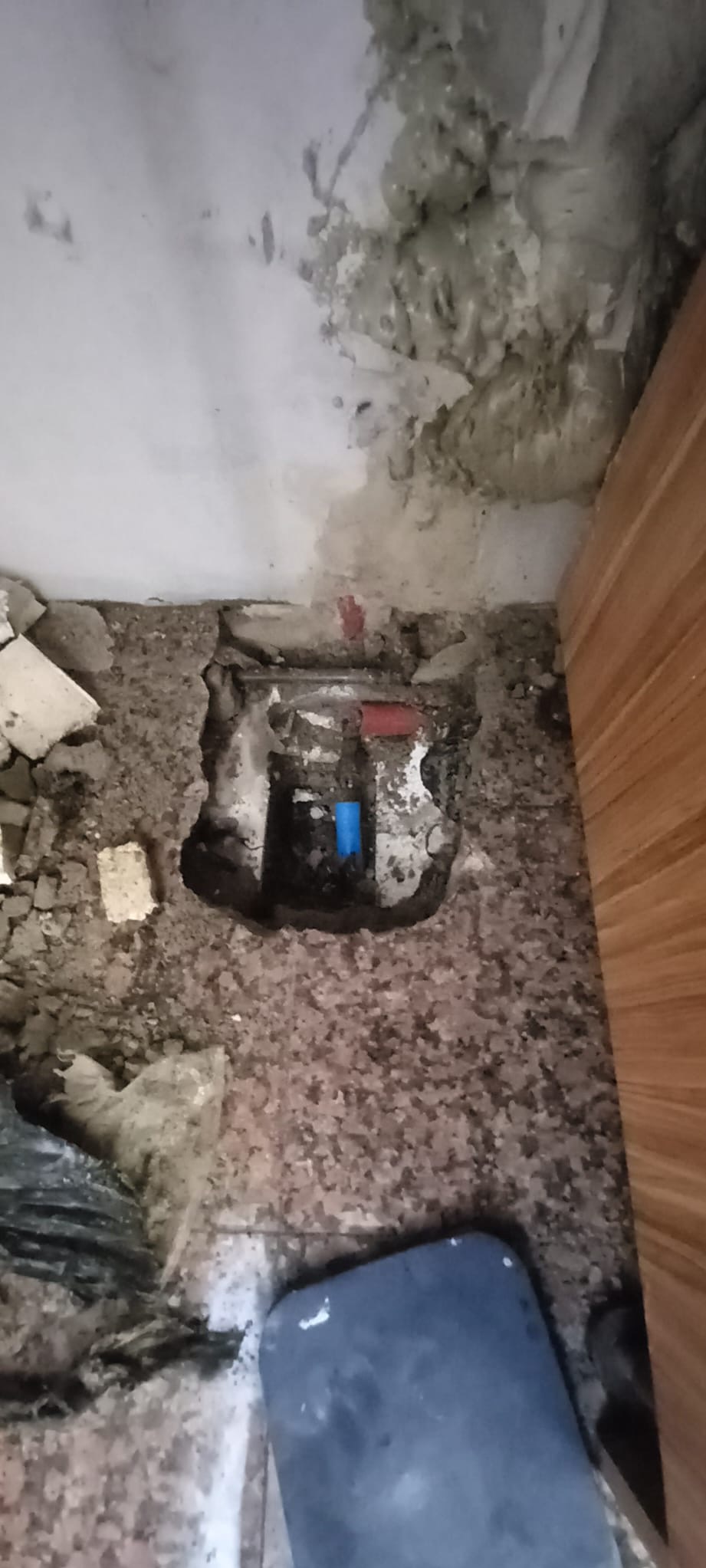 Odkryte rury wodne w ścianie z uszkodzonym tynkiem, widoczne fragmenty niebieskiej i czerwonej instalacji, w tle ślady wilgoci na suficie.