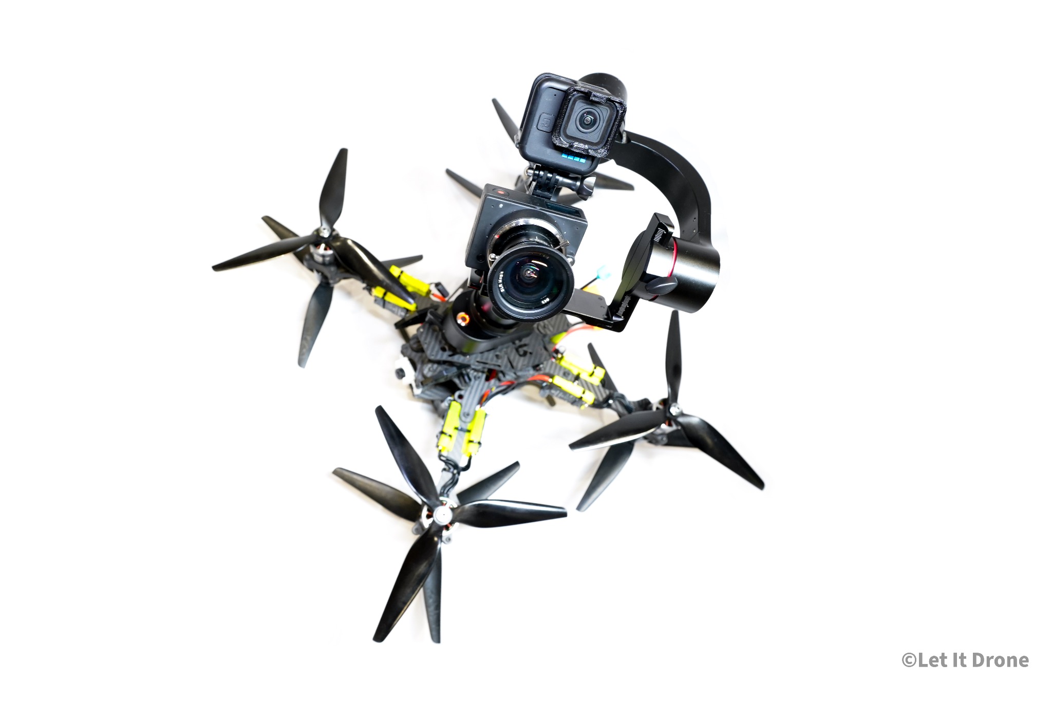 Profesjonalny dron z zamontowanymi dwiema kamerami, w tym GoPro, na białym tle, widoczne czarne śmigła i elementy konstrukcyjne z żółtymi akcentami.
