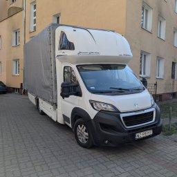 Serhii Kovela Przewóz - Biały bus z plandeką 'Dream Master' na tle bloku mieszkalnego. Pojazd zaparkowany na chodniku z kostki brukowej. Widoczna tablica rejestracyjna WZ 989HV.