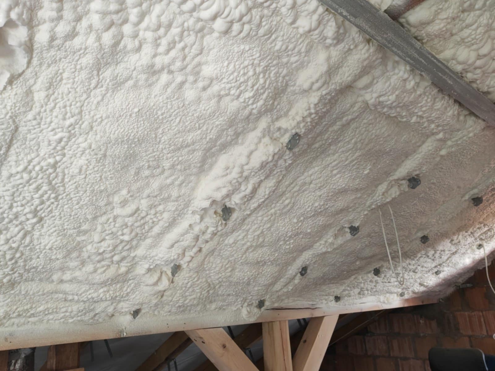 Poddasze ocieplone białą pianką poliuretanową, widoczne drewniane elementy konstrukcyjne i metalowe mocowania.