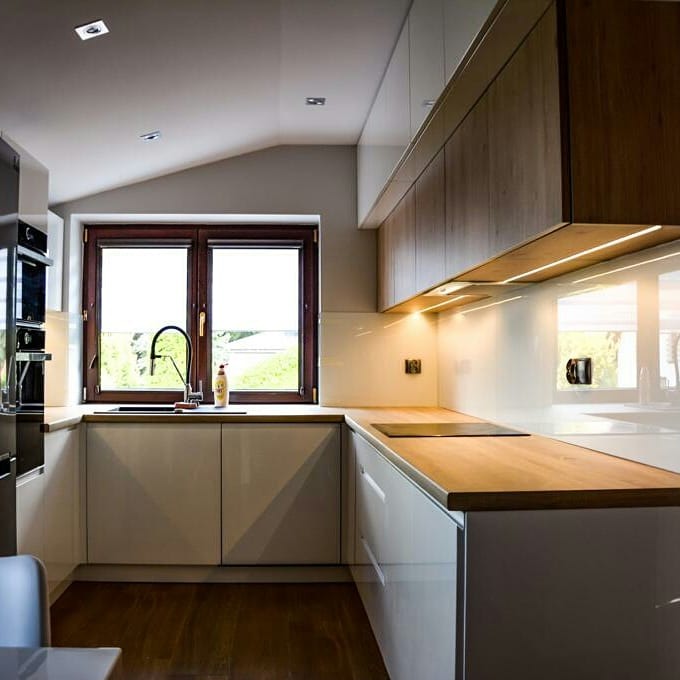 Jasna kuchnia z drewnianymi blatami i białymi szafkami, okno z widokiem na zieleń. Podświetlenie LED pod szafkami górnymi. Nowoczesny design.