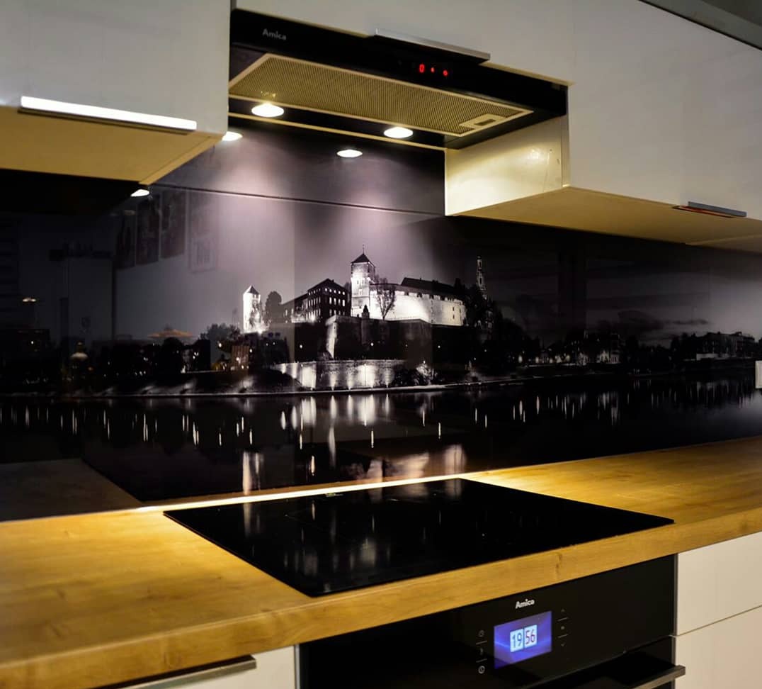 Szklany panel kuchenny z motywem czarno-białego krajobrazu miejskiego, zamek odbijający się w wodzie. Nowoczesna kuchnia z drewnianym blatem i płytą indukcyjną.