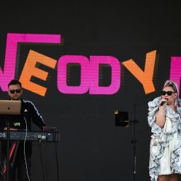 Patrycja Neodym - Występ zespołu Neodym: kobieta w srebrnej sukience śpiewa do mikrofonu, obok mężczyzna gra na keyboardzie Korg Kronos z laptopem na tle neonowego logo.