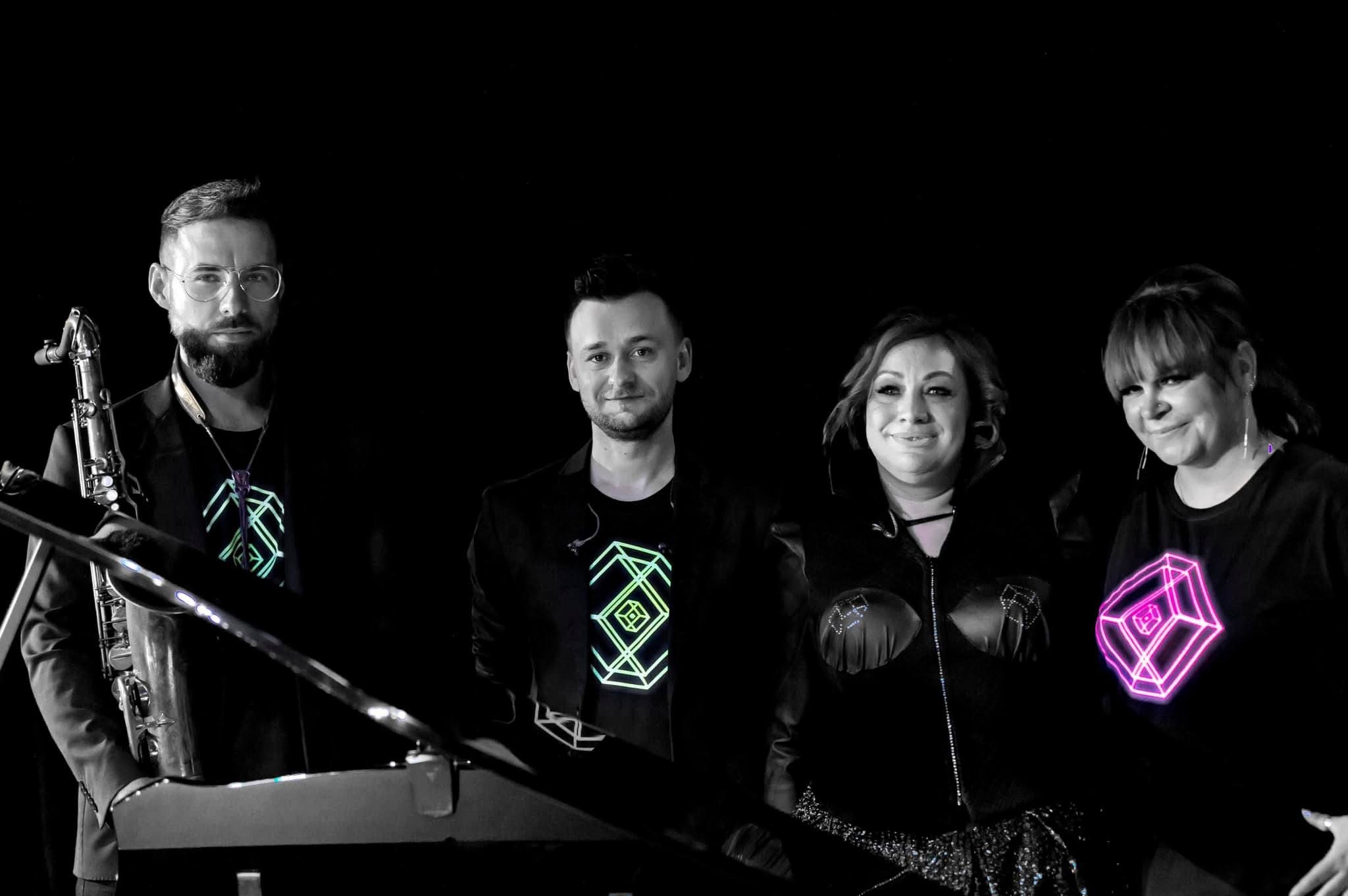 Zespół muzyczny w czarnych strojach z geometrycznymi, neonowymi wzorami na koszulkach, saksofonista po lewej, klawiszowiec i dwie wokalistki na czarnym tle.