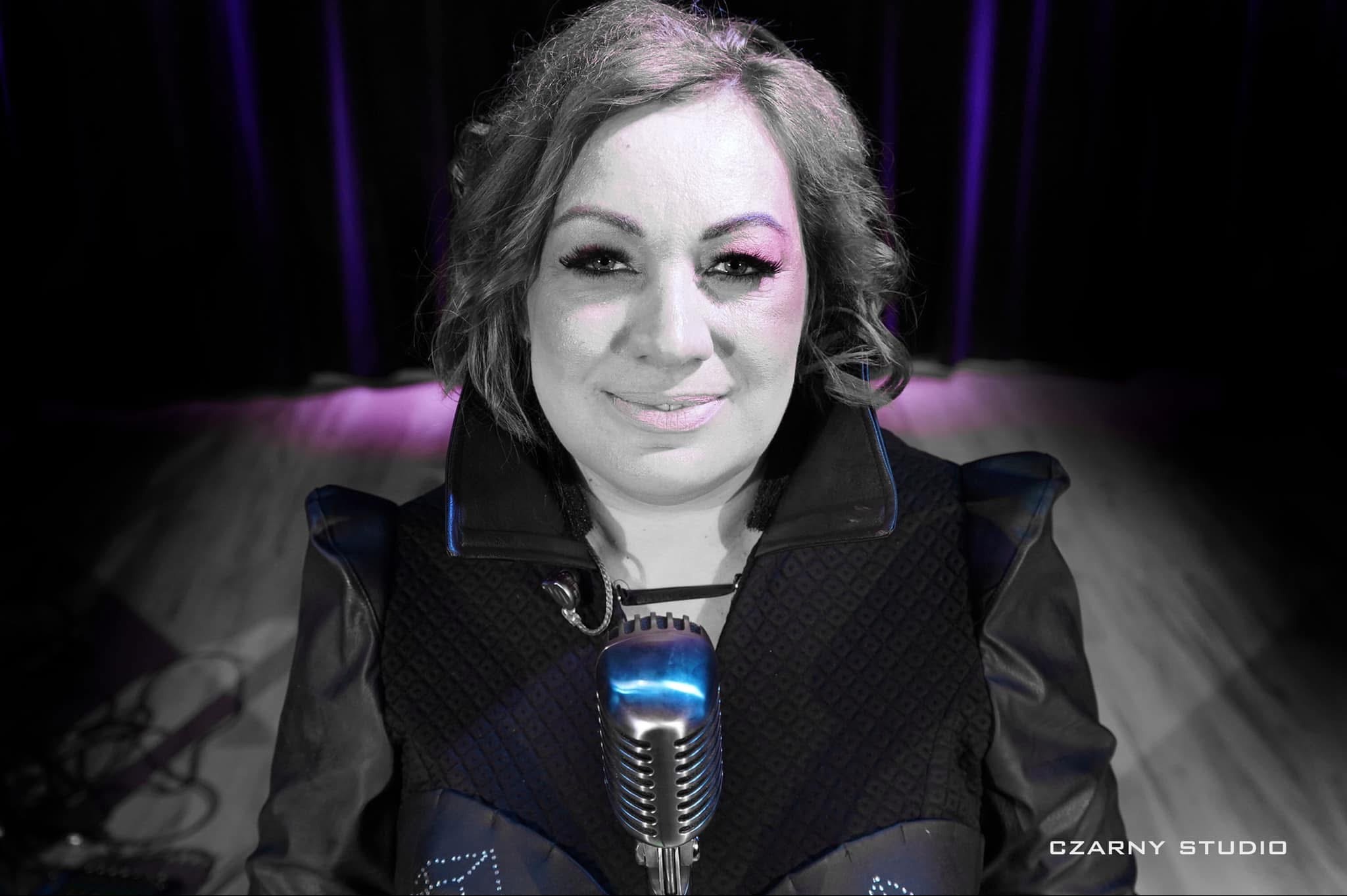Portret kobiety z mikrofonem w stylu retro, na scenie z fioletowym oświetleniem. Czarno-biała tonacja z kolorowymi akcentami.