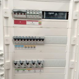 PPHU LionSystems Dmytro Stasiuk - Biała skrzynka elektryczna z bezpiecznikami i wyłącznikami firmy Legrand, widoczne oznaczenia Q1-Q13 i diody sygnalizacyjne.