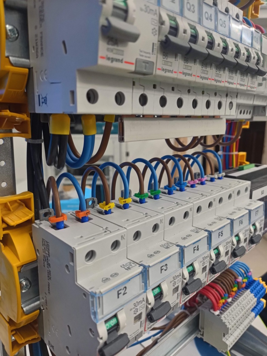 Szczegółowe ujęcie tablicy rozdzielczej z bezpiecznikami i okablowaniem, widoczne kolorowe oznaczenia przewodów i elementy montażowe.