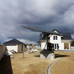 P3Elektro z o.o - Montaż wysięgnika z panelami fotowoltaicznymi na posesji z nowym domem jednorodzinnym, widoczny pracownik przy konstrukcji i osoba wchodząca do domu.