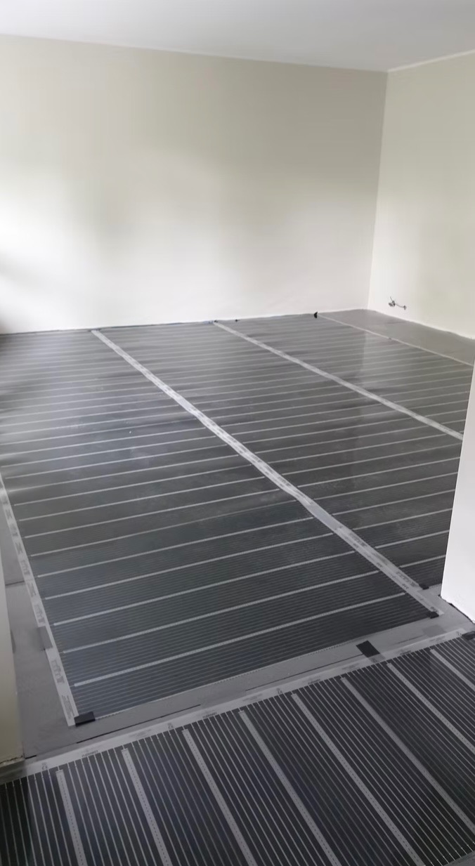 Rozłożona mata grzewcza pod wylewkę w pustym pomieszczeniu, widoczne łączenia i przewody elektryczne.