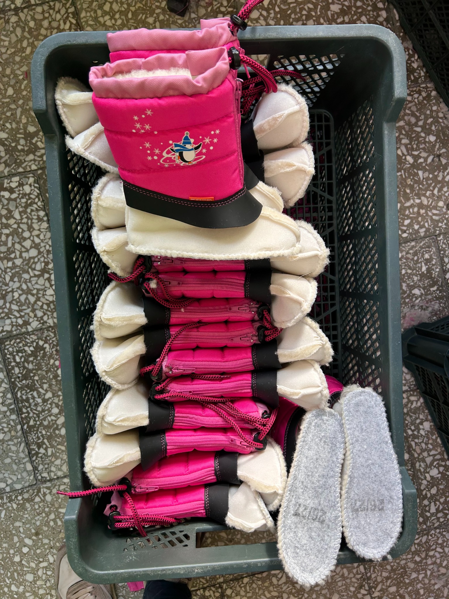 Różowe, dziecięce buty zimowe z białym futerkiem i motywem pingwina, ułożone w szarym koszu w firmie z Łącka, widoczne również szare wkładki do butów.
