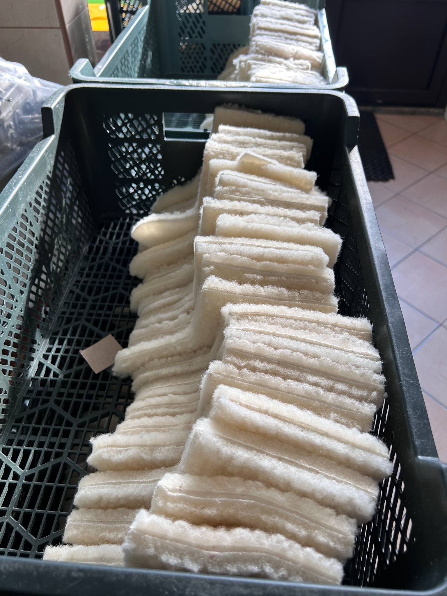 Rząd ułożonych, białych, puszystych wkładów w zielonej, plastikowej skrzynce, prawdopodobnie przeznaczonych do szycia pościeli lub pokrowców.