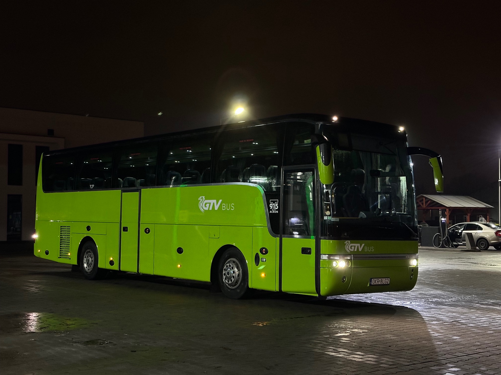 Zielony autokar GTV Bus stoi na parkingu nocą, oświetlony reflektorami, widoczny numer rejestracyjny OKR 8LG2.