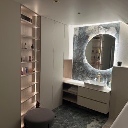 MARIUSZ LEWKIEWICZ - Nowoczesna łazienka na poddaszu z szafkami na wymiar, okrągłym lustrem z podświetleniem LED i marmurową posadzką. Widoczny fragment wanny i pufa.