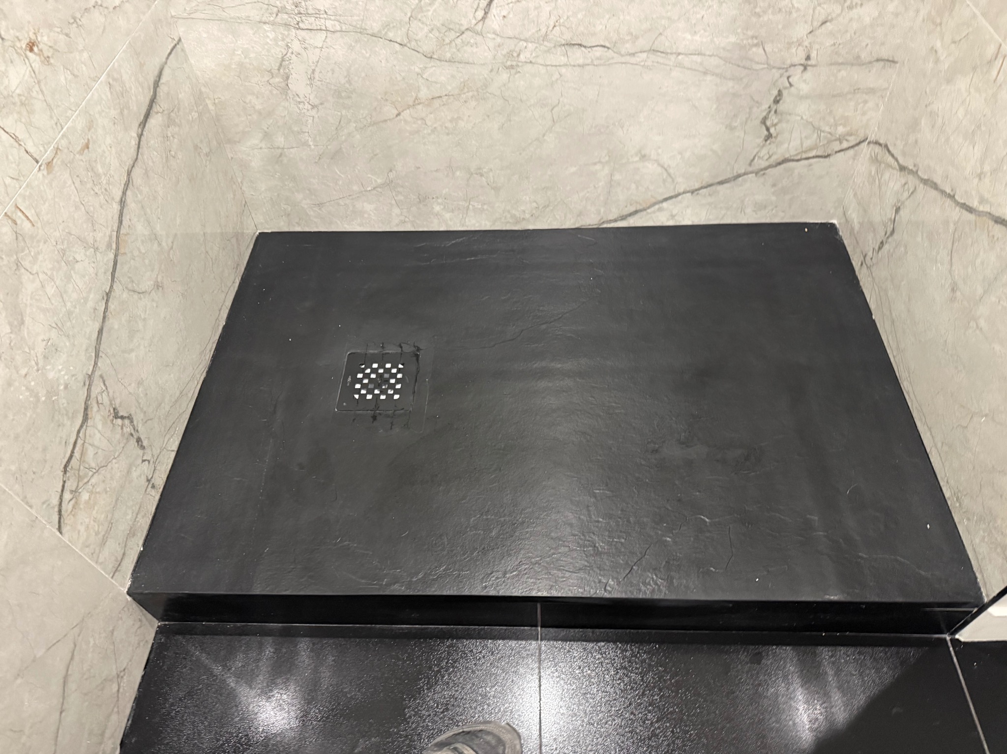 Czarny brodzik z odpływem liniowym, otoczony marmurowymi płytkami. Widok z góry, podkreślający minimalistyczny design i precyzję wykonania.