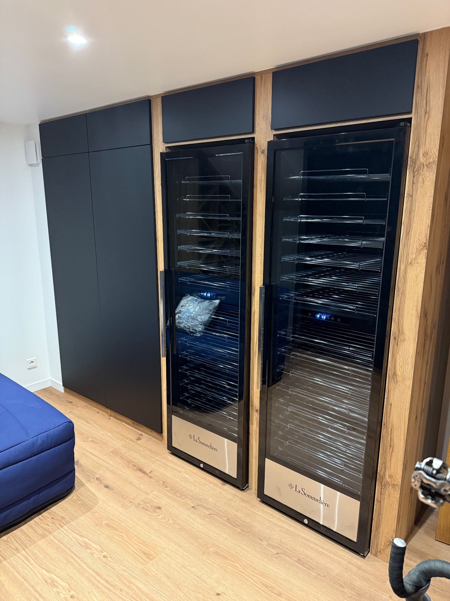 Nowoczesna zabudowa: czarne szafy i dwie chłodziarki do wina La Sommeliere z drewnianymi panelami bocznymi, na podłodze panele imitujące drewno.