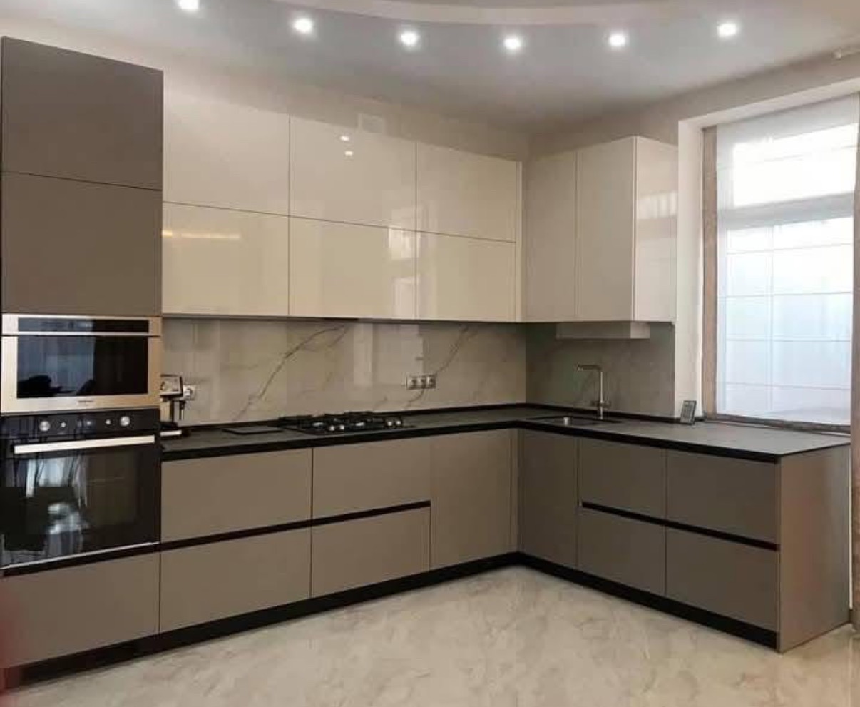 Nowoczesna kuchnia w kształcie litery L z beżowymi i szarymi frontami, czarnym blatem i marmurowym backsplashiem. Wbudowany piekarnik i płyta gazowa.