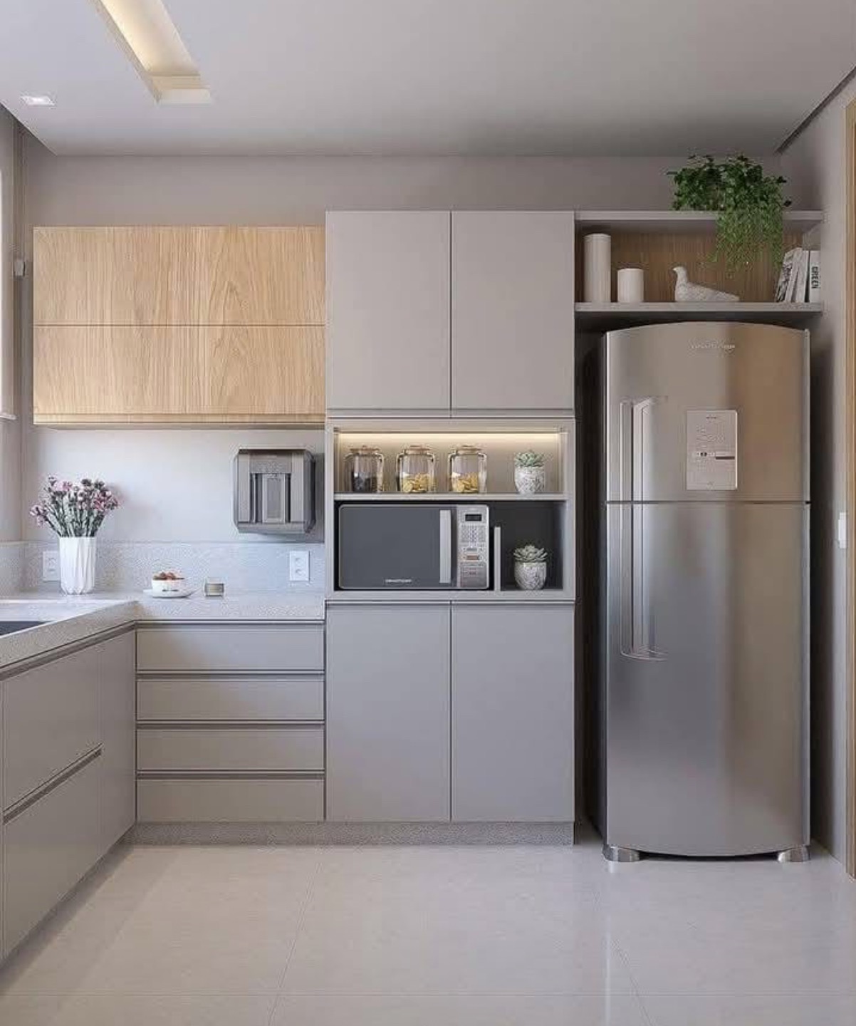 Nowoczesna kuchnia z szarymi szafkami, drewnianymi akcentami i srebrną lodówką. Minimalistyczny design z roślinami doniczkowymi i oświetleniem LED.