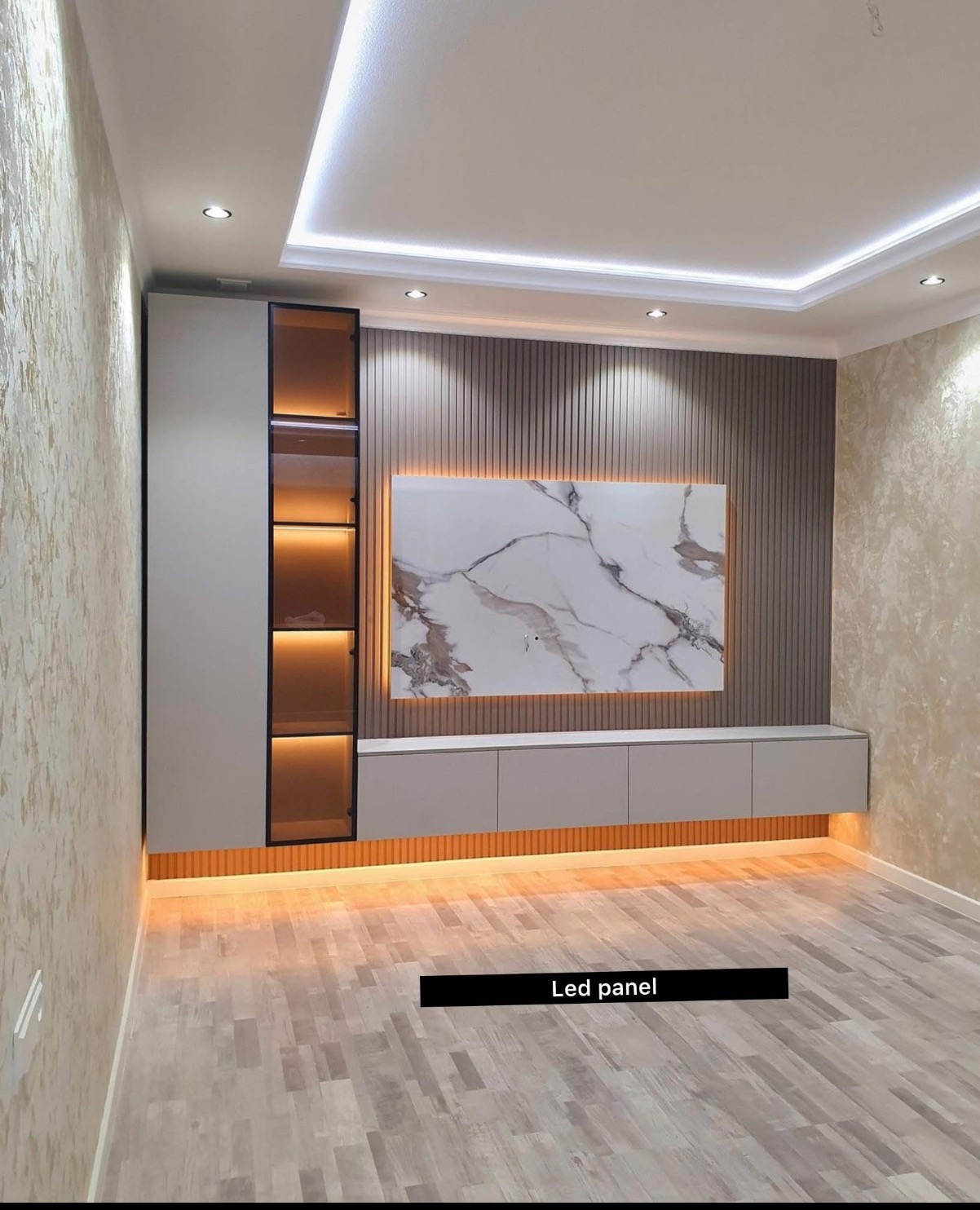 Nowoczesny salon z podświetlaną ścianą TV, szafką RTV i wysoką szafą z półkami. Dekoracyjna ściana z panelem imitującym marmur i oświetleniem LED.