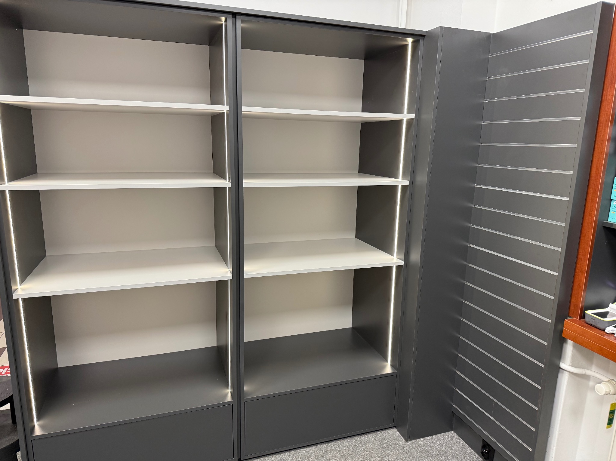 Szare, podświetlane półki z białymi wnękami, część ekspozycji meblowej z panelami ściennymi na metalowe zawieszki, widok z dołu.