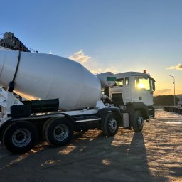 DROG-TECH SPÓŁKA Z OGRANICZONĄ ODPOWIEDZIALNOŚCIĄ - Czysta, biała betonomieszarka na placu budowy oświetlona zachodzącym słońcem, z widocznymi formami betonowymi w tle.