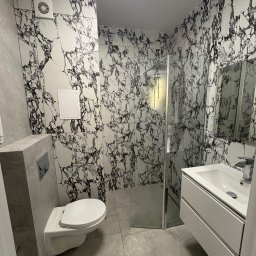 Andrii Nesen Master Bud - Nowoczesna łazienka z kabiną prysznicową, umywalką z szafką i podwieszaną toaletą. Ściany i podłoga wyłożone płytkami imitującymi marmur.