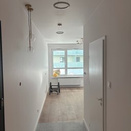 Andrii Nesen Master Bud - Nowoczesny korytarz z panelami podłogowymi przechodzącymi w szare płytki, białe ściany i sufit z trzema designerskimi lampami. Widoczne okno z widokiem na budynek.