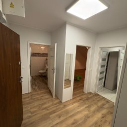 Andrii Nesen Master Bud - Jasne wnętrze mieszkania po remoncie: drewnopodobne panele podłogowe, białe ściany i drzwi, widok na łazienkę i inne pomieszczenia. Nowoczesne oświetlenie sufitowe.