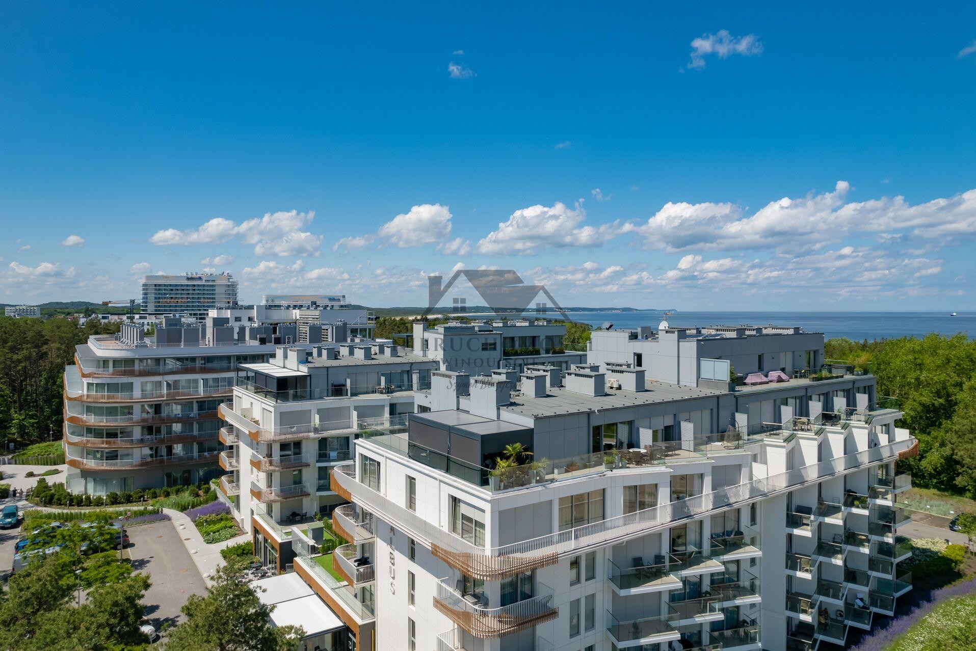 Nowoczesny kompleks apartamentów z balkonami i widokiem na morze pod błękitnym niebem z chmurami, Świnoujście. Widok z góry na budynki i zieleń.