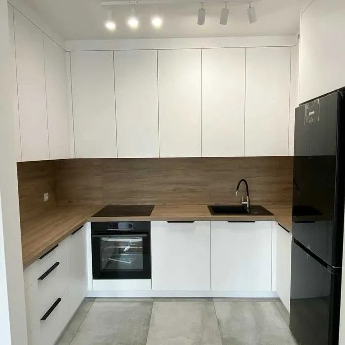 Nowoczesna kuchnia w kształcie litery U: białe szafki, drewniany blat, czarny zlew i sprzęt AGD. Minimalistyczny design z oświetleniem punktowym.