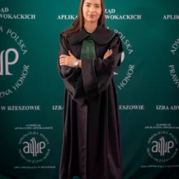 Portret młodej kobiety w todze adwokackiej, na tle z logo Izby Adwokackiej w Rzeszowie, z zegarkiem na nadgarstku i czarnych szpilkach.