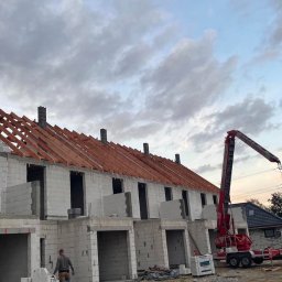 WIKING PRO sp. z o.o. - Budowa szeregu domów jednorodzinnych w stanie surowym otwartym, widoczne bloczki z betonu komórkowego, drewniana konstrukcja dachu, dźwig budowlany w tle, pochmurne niebo.