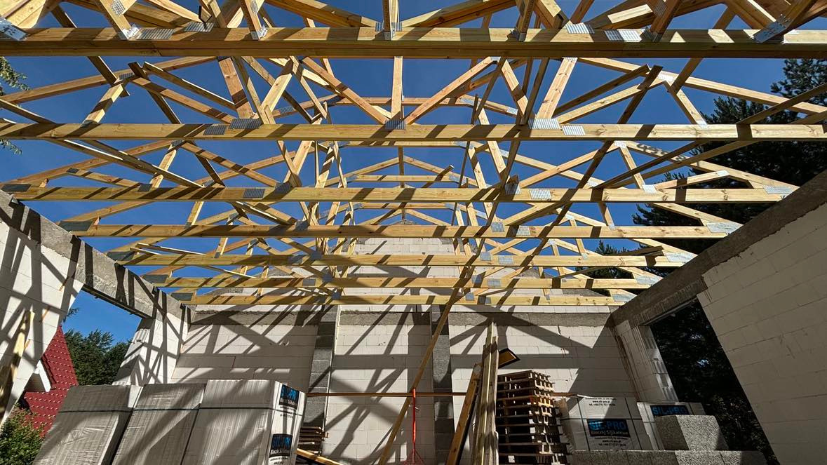 Wznoszenie drewnianej konstrukcji dachu na budynku z betonu komórkowego, widoczne pakiety bloczków SILKA PRO, jasne drewno konstrukcyjne na tle błękitnego nieba.