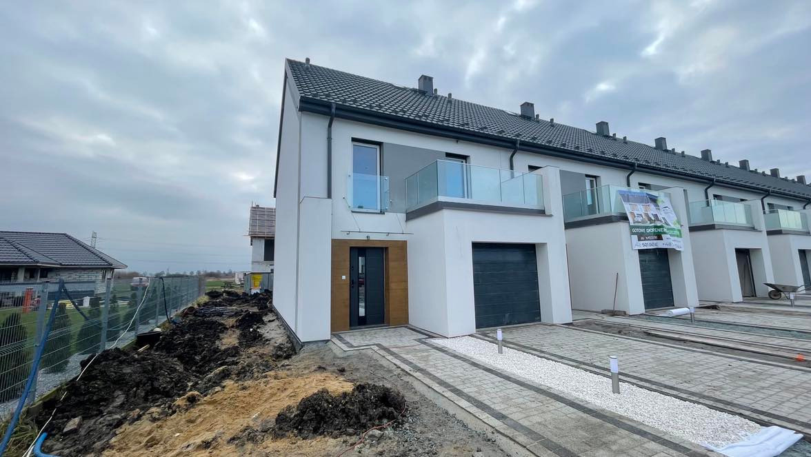 Nowoczesne szeregowe domy z płaskimi dachami i szklanymi balkonami, widoczne prace wykończeniowe terenu wokół budynków.