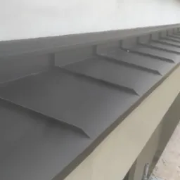 Nowoczesne, czarne obróbki blacharskie na dachu budynku, widoczne z rusztowania. Kąt ujęcia podkreśla geometrię i precyzję wykonania.