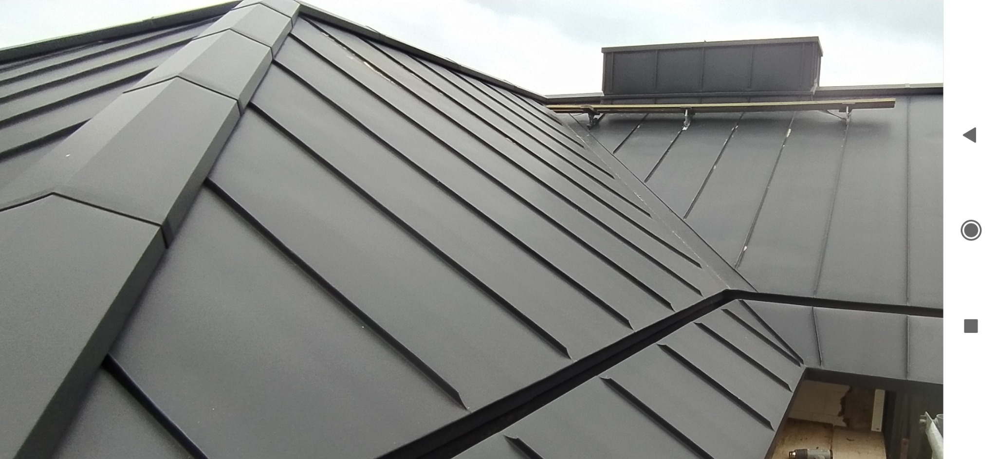 Szczegółowe ujęcie grafitowego dachu z blachy na rąbek stojący. Widoczne precyzyjne łączenia i elementy wentylacyjne. Nowoczesne pokrycie dachowe.