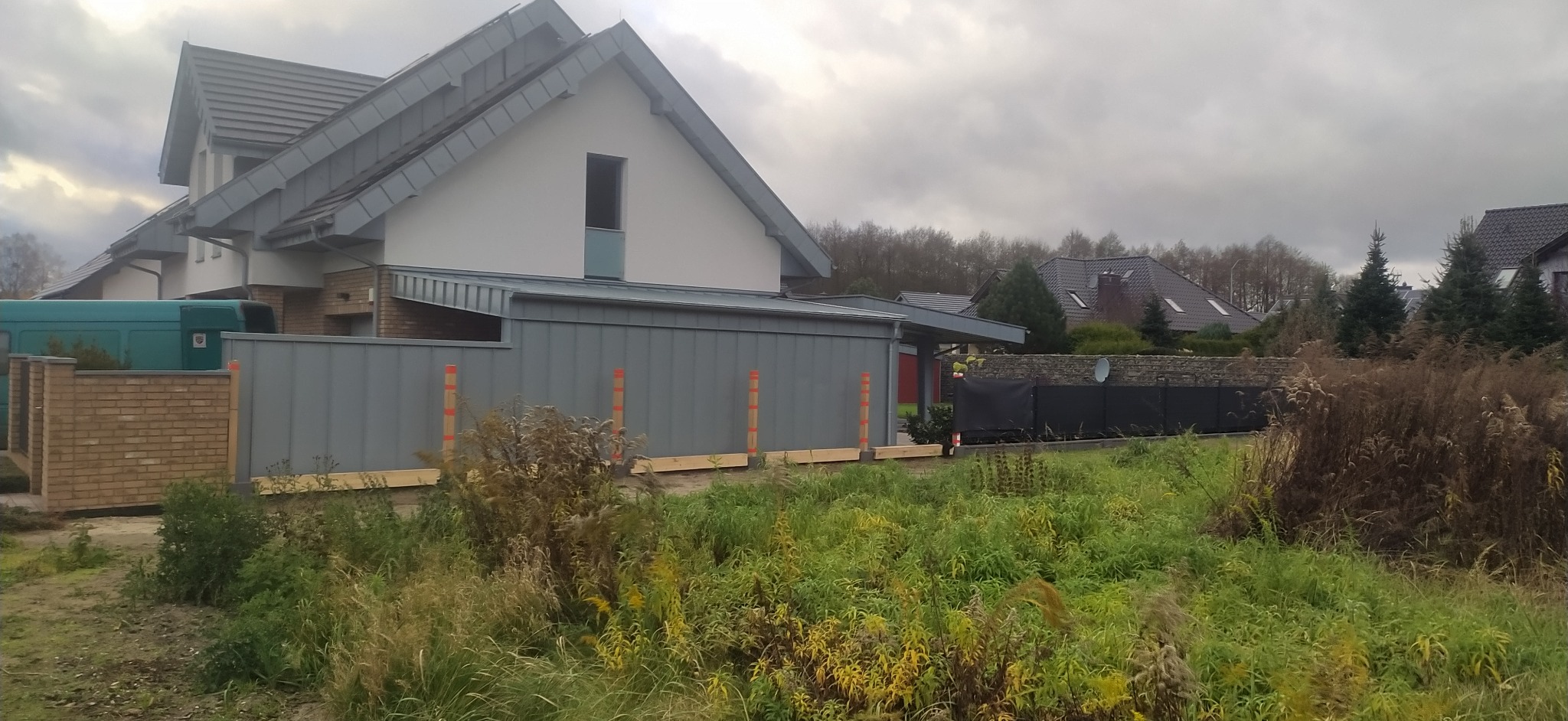 Szary dach z blachy na nowoczesnym domu jednorodzinnym, widok z poziomu gruntu, pochmurne niebo w tle. Elementy obróbki blacharskiej.