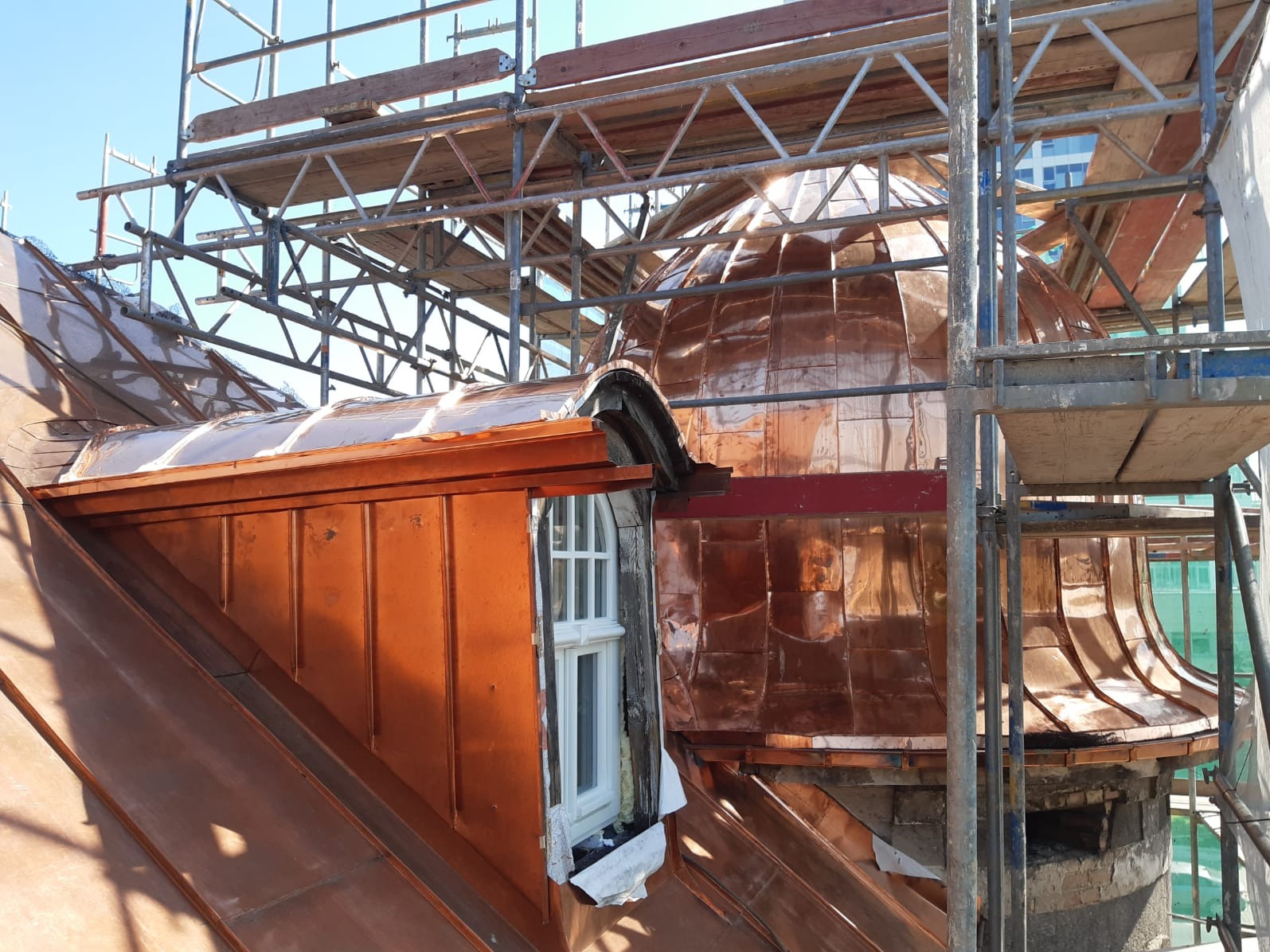 Miedziane pokrycie dachu kopuły, rusztowania w tle. Prace dekarskie w Szczecinie. Widoczne detale obróbek blacharskich i okna dachowe w trakcie montażu.
