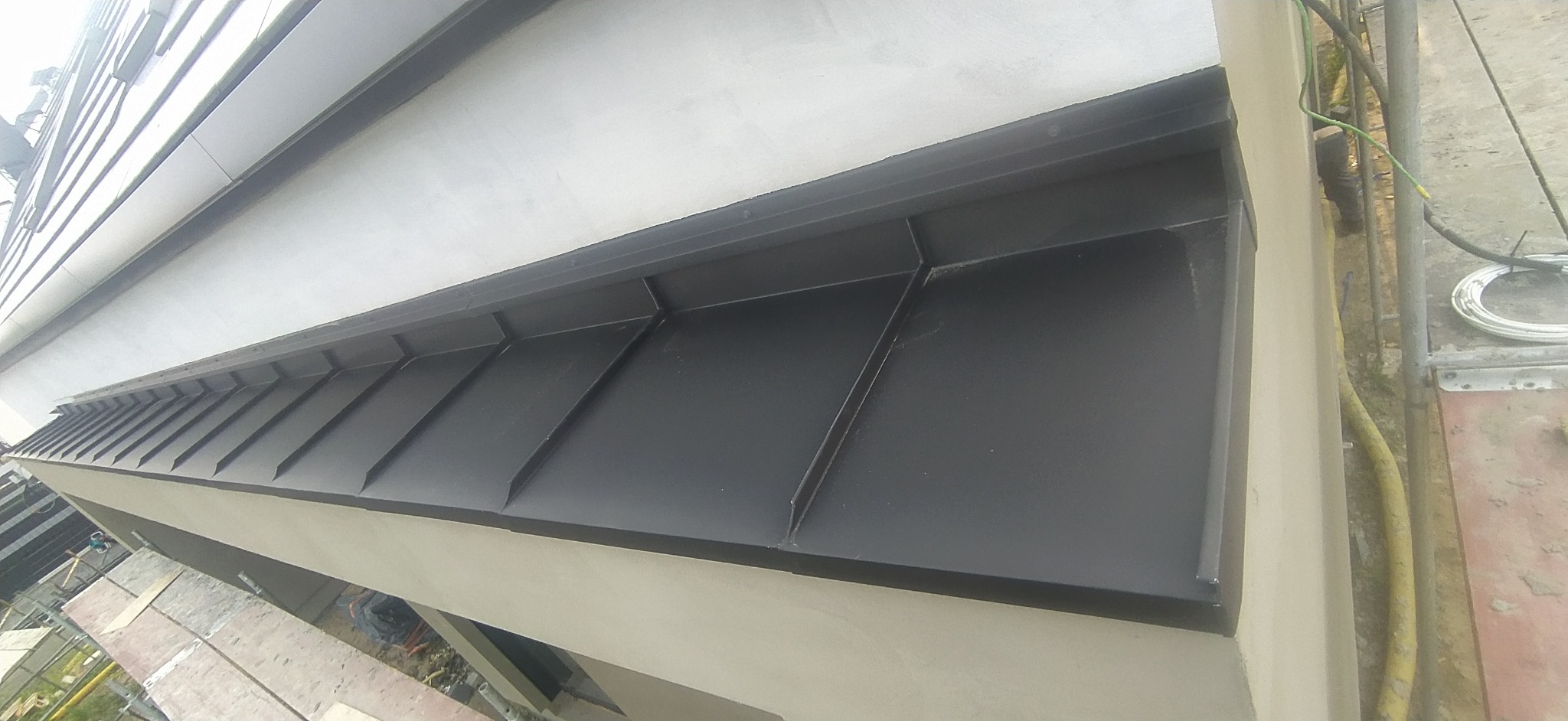 Szara blacha na dachu budynku z widocznymi elementami konstrukcyjnymi i przewodami. Dach pokryty blachą na gotowo.