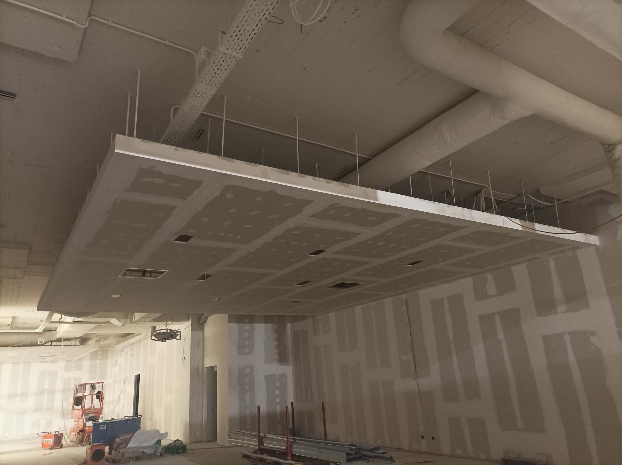 Montaż podwieszanego sufitu z płyt gipsowo-kartonowych w biurze, widoczne profile i instalacje pod sufitem, ściany w stanie surowym.