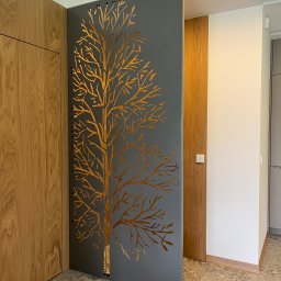 Dekory z metalu - Metalowa ścianka działowa z wyciętym wzorem drzewa, oddzielająca przestrzeń w nowoczesnym wnętrzu z drewnianymi elementami i oświetleniem LED.
