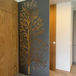 Metalowa ścianka działowa z wyciętym wzorem drzewa, oddzielająca przestrzeń w nowoczesnym wnętrzu z drewnianymi elementami i oświetleniem LED.