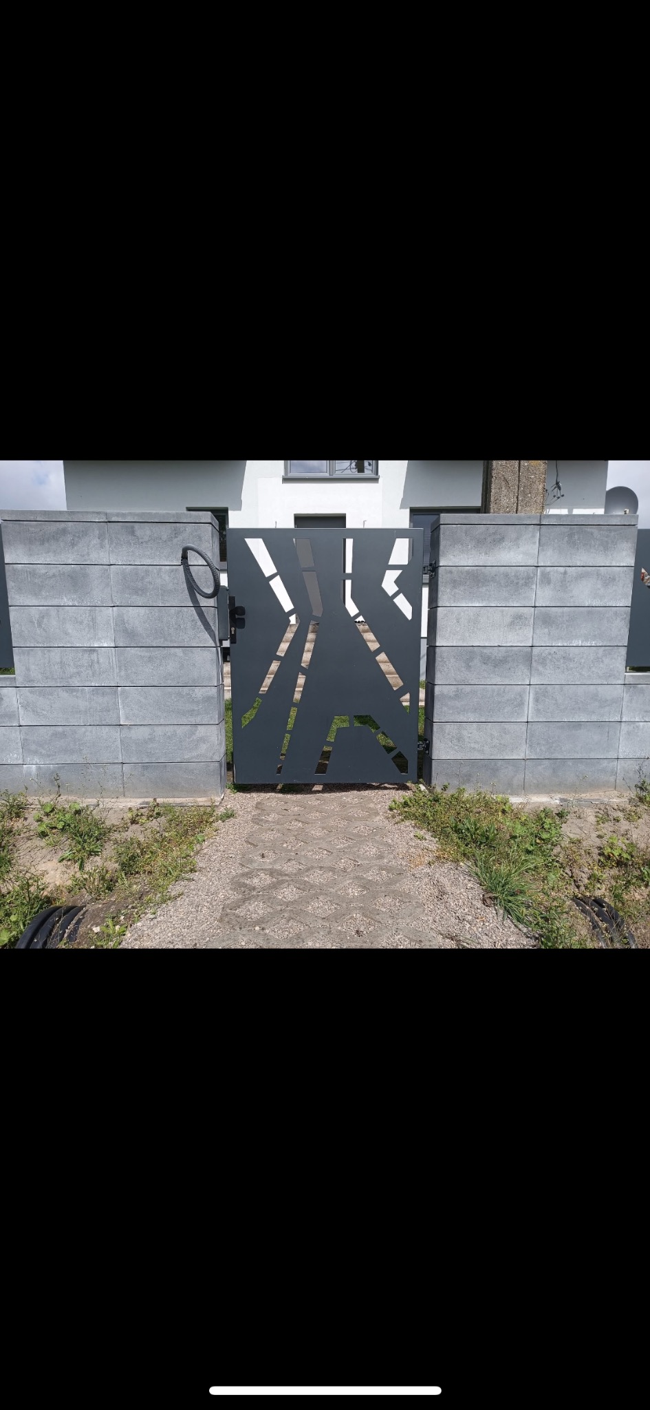 Nowoczesna brama wjazdowa z geometrycznym wzorem wyciętym laserowo, zamontowana między betonowymi słupkami ogrodzenia.