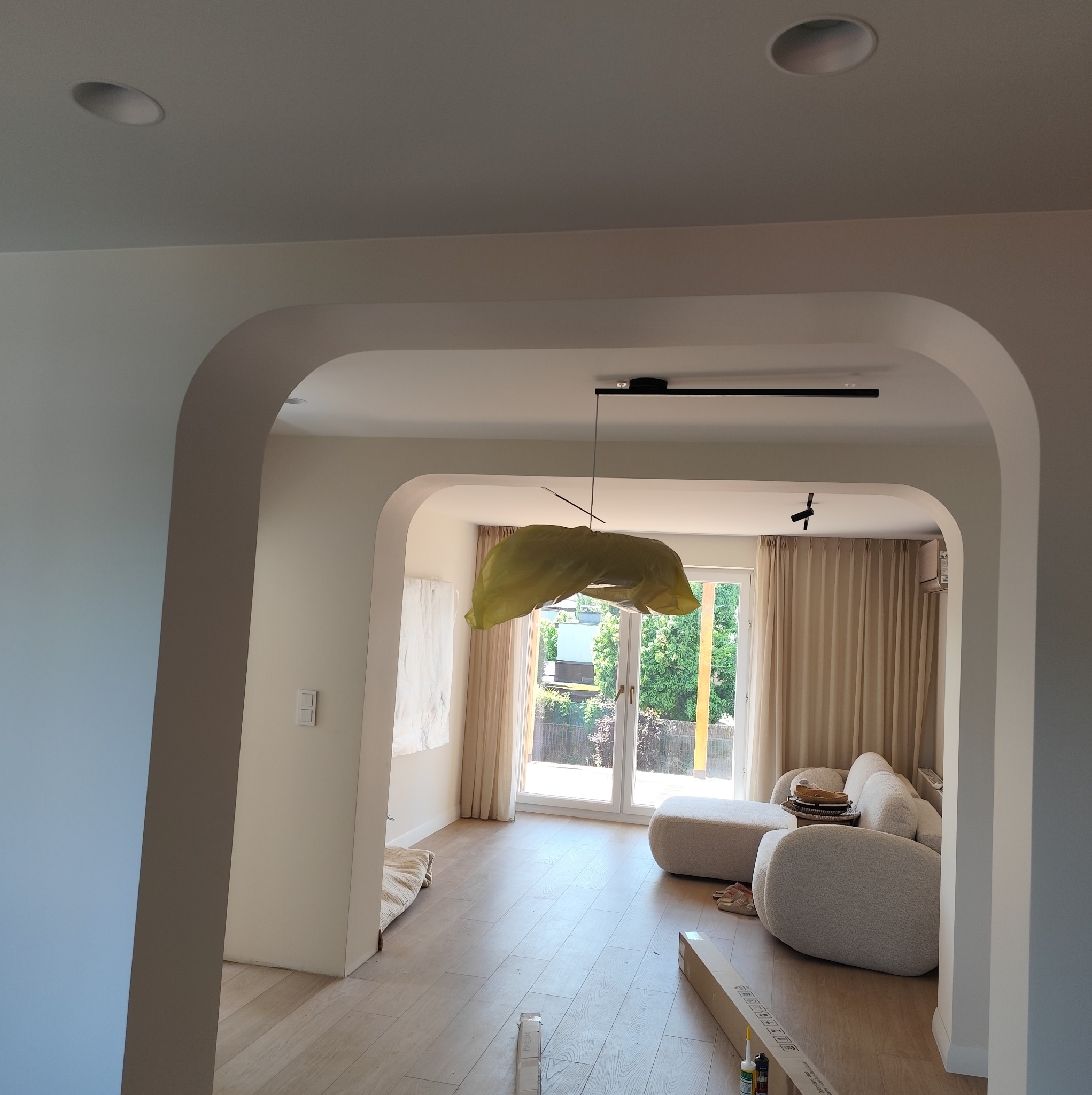 Wnętrze po odświeżeniu z łukowym przejściem i nowym oświetleniem. Lampa wisząca zabezpieczona folią malarską. Widoczne kartony i akcesoria na podłodze.