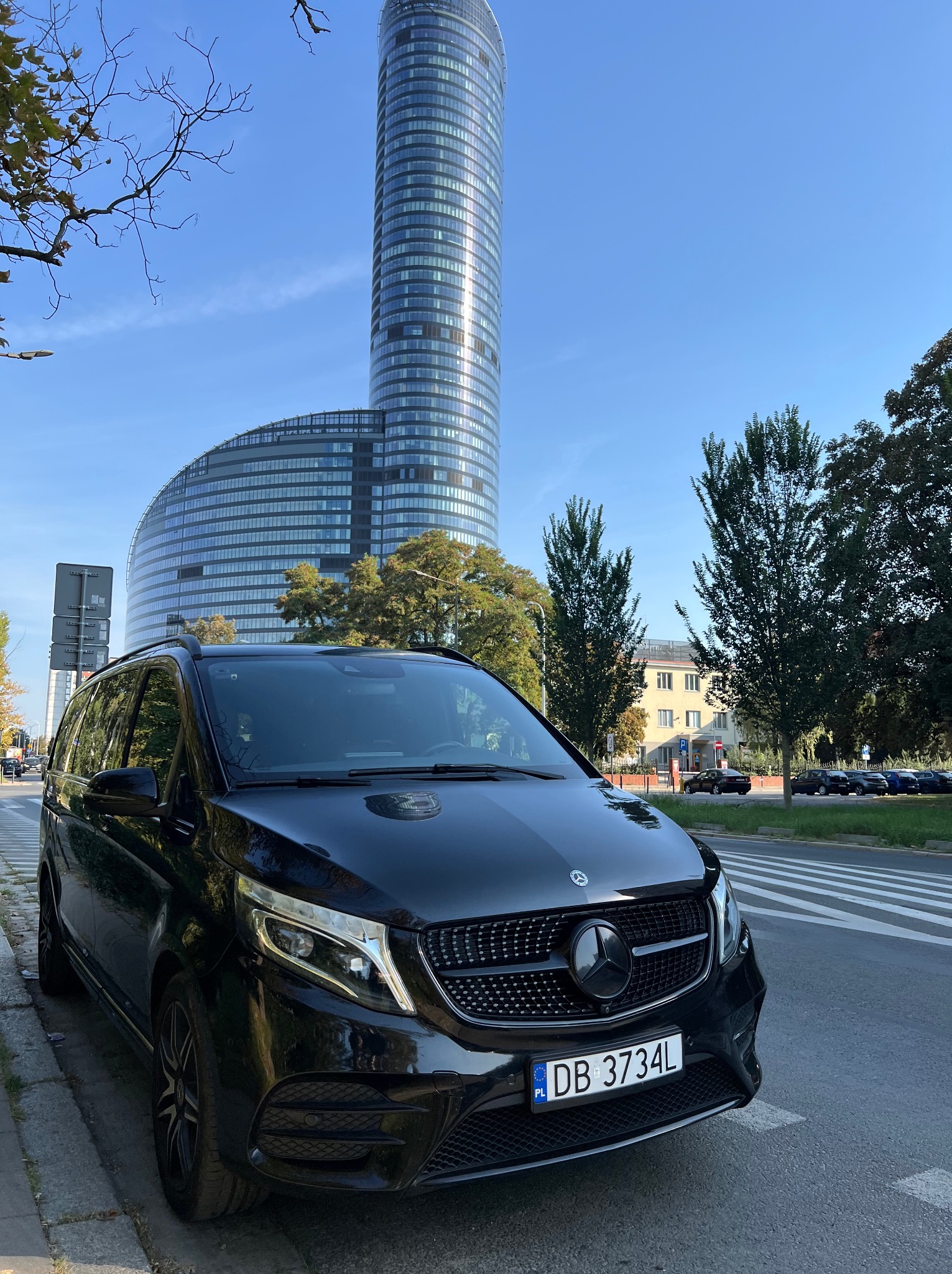 Czarny Mercedes-Benz Vito z polskimi tablicami rejestracyjnymi DB 3734L zaparkowany na tle nowoczesnego wieżowca w Katowicach.